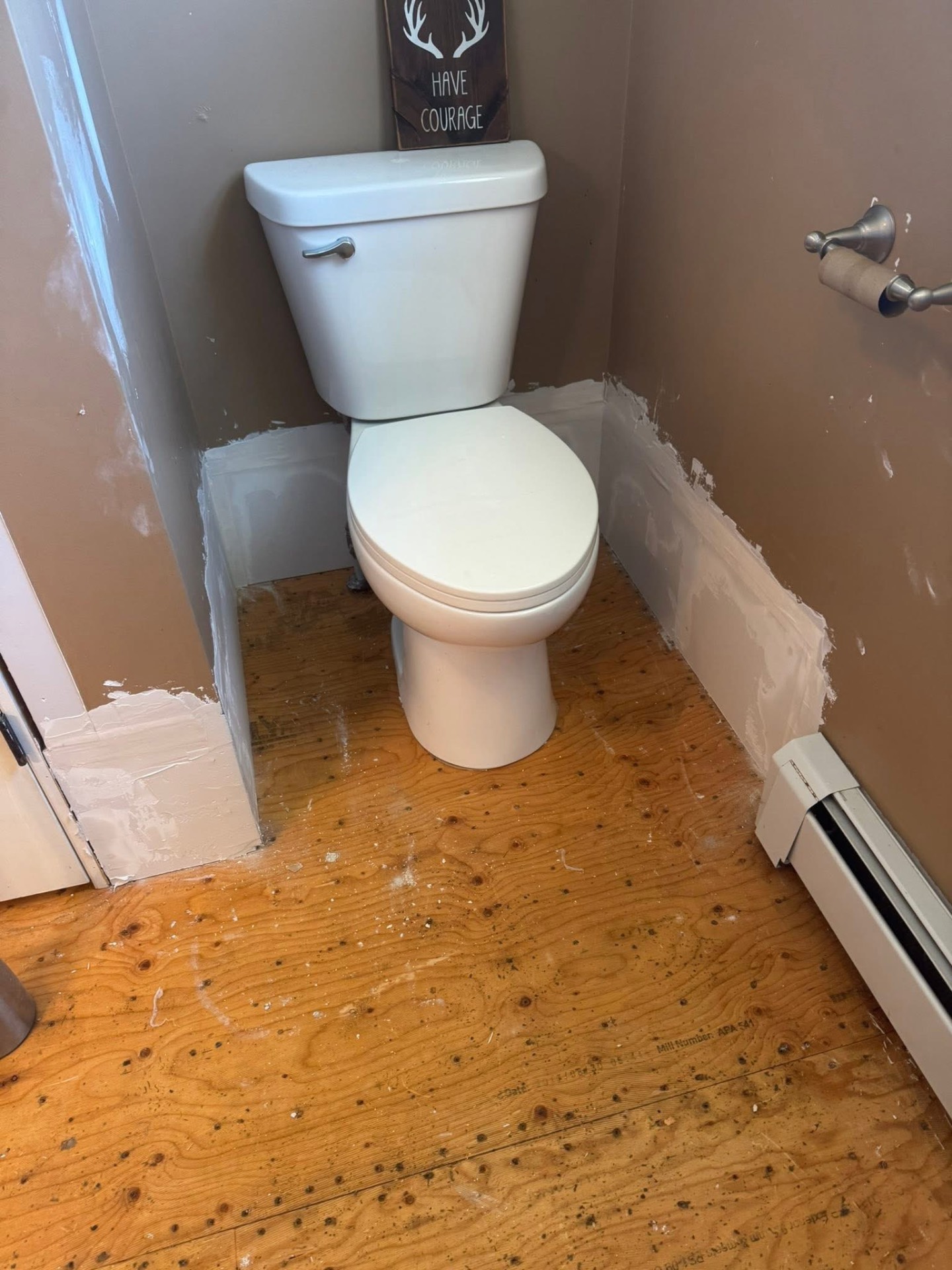 Bathroom with exposed plywood subfloor and patched drywall