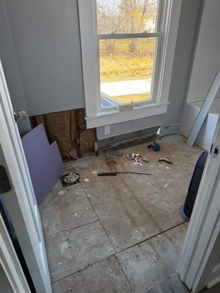 Small bathroom stripped to subfloor with exposed plumbing
